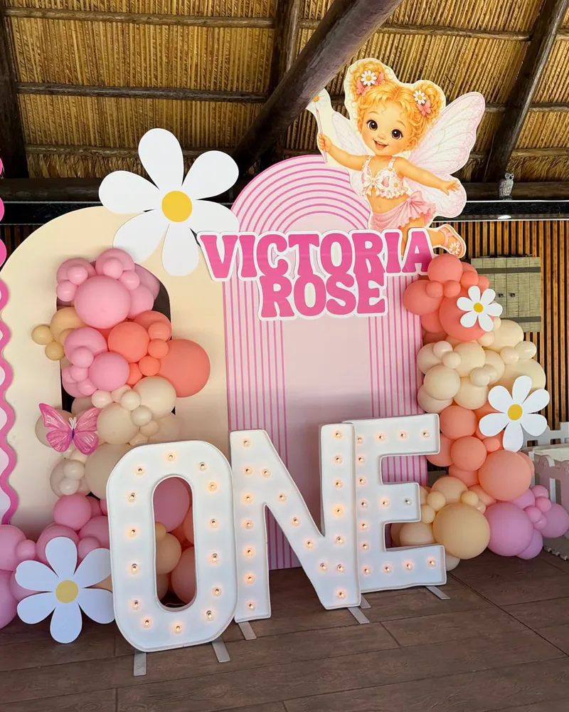 First birthday setup with light-up ONE letters, daisy cutouts and a coral balloon garland