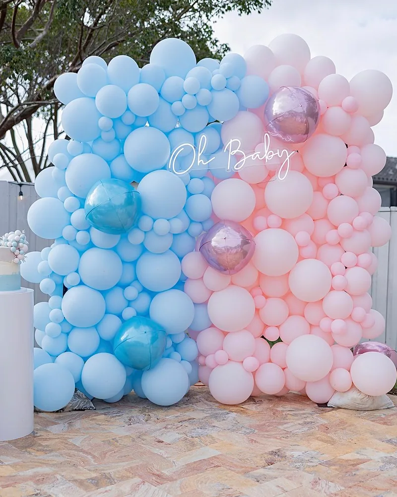 Gender reveal balloon wall, half blue and half pink, with an Oh Baby neon sign