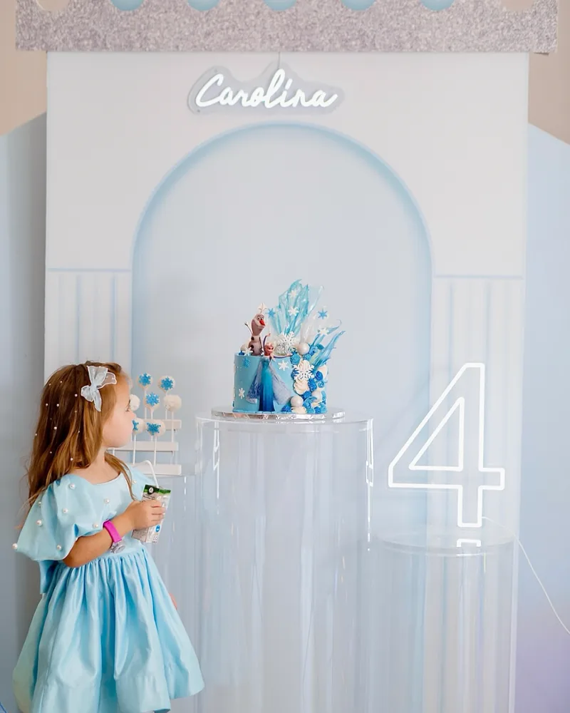 Frozen themed fourth birthday with an ice blue backdrop, a neon name sign and acrylic plinths