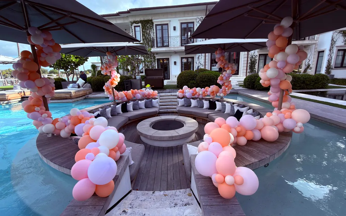 Waterfront estate with balloon garlands wrapped around the umbrellas of a sunken poolside lounge