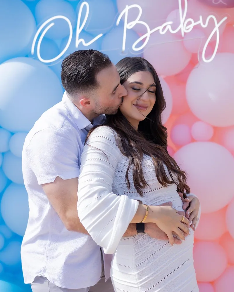 Expecting parents in front of the blue and pink Oh Baby gender reveal balloon wall