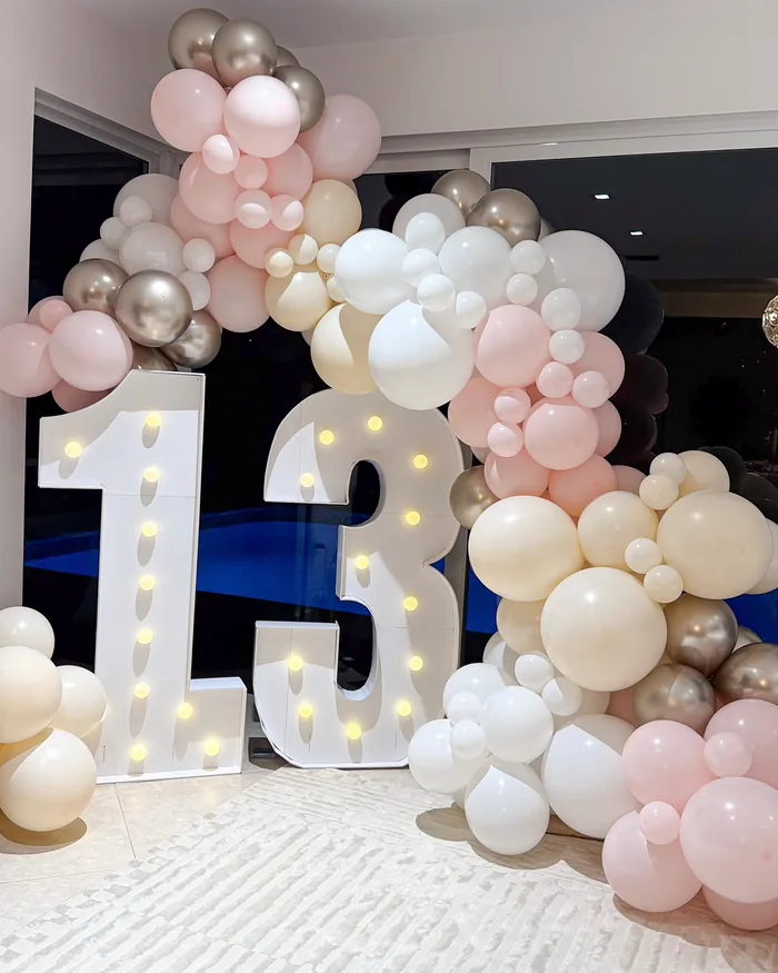 A light-up marquee number beside a balloon garland, available for rental